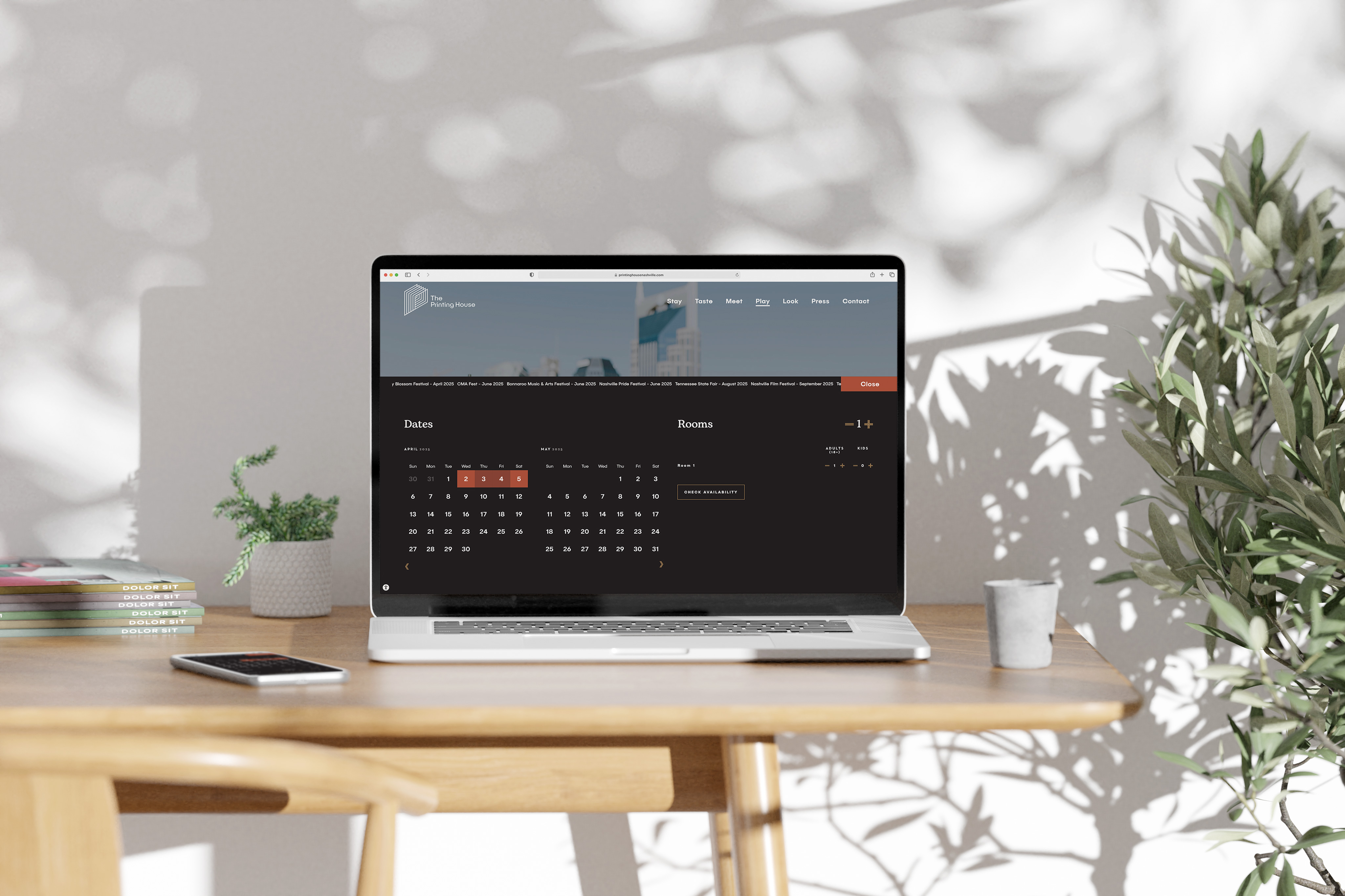 A laptop on a wooden desk displays a hotel booking calendar. Nearby are a small plant, a smartphone, a white cup, and a larger plant in the background. Sunlight casts shadows on the wall.