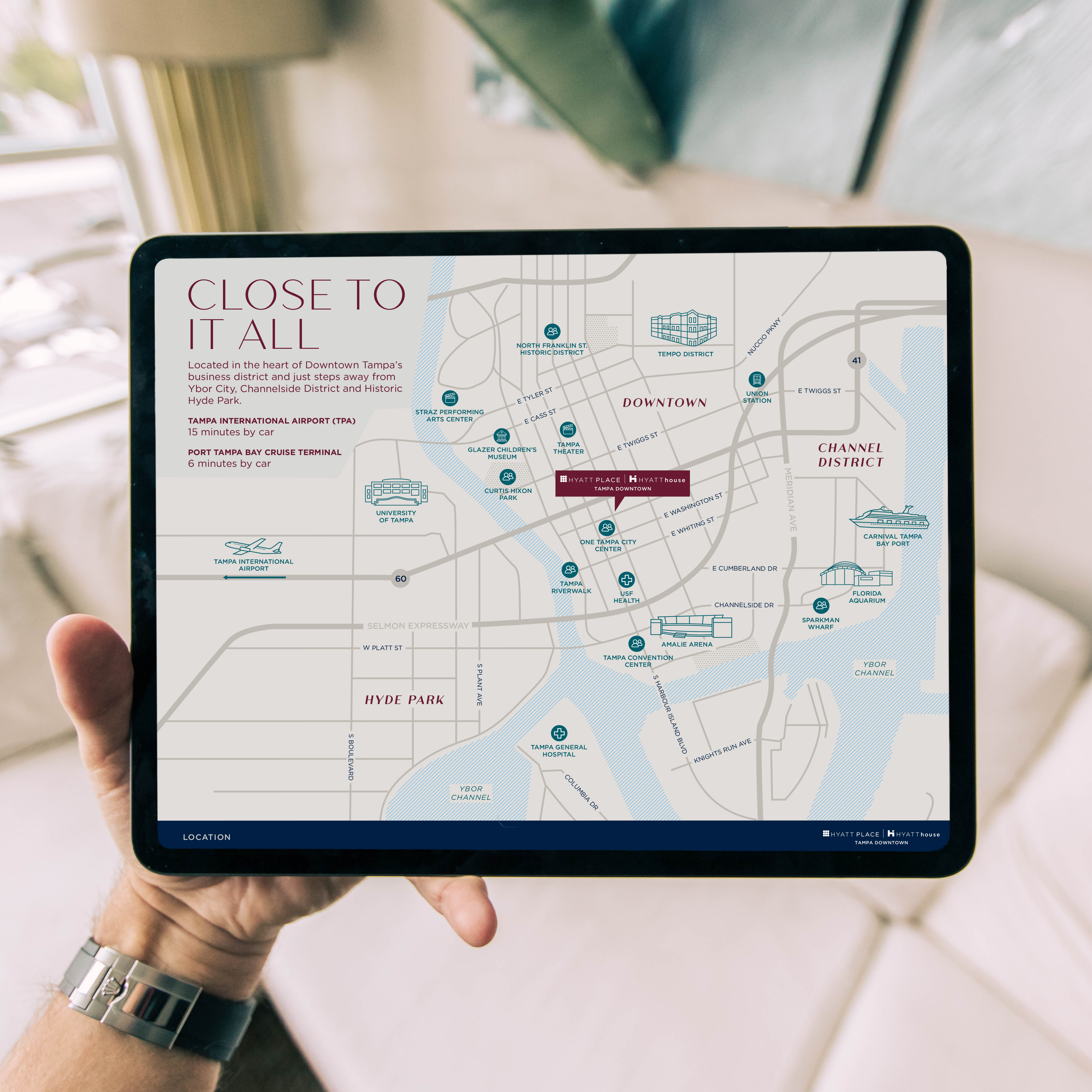 A hand holds a tablet displaying a map titled "Close To It All," featuring turnkey directions to key locations in downtown Tampa and surrounding districts.